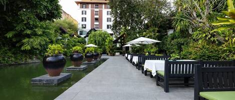 A pathway lined with tables and chairs, a water feature, and a building in the background.