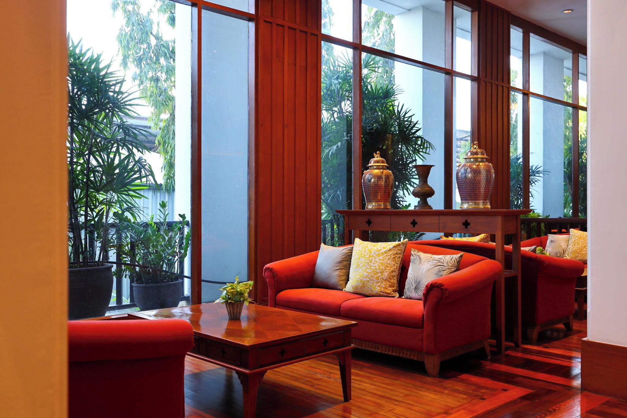 Una habitación amplia con ventanas grandes, un sofá rojo, una mesa de centro de madera y jarrones decorativos.