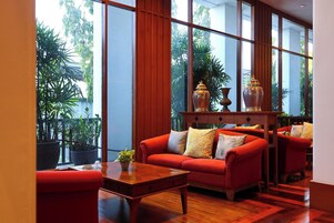 Una habitación amplia con ventanas grandes, un sofá rojo, una mesa de centro de madera y jarrones decorativos.