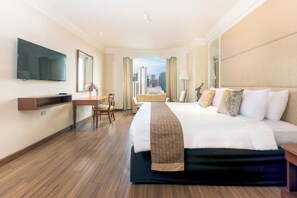 A hotel room with a large bed, a desk, a chair, a TV, and a view of the cityscape.