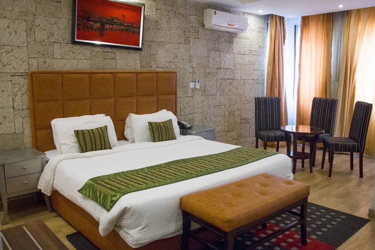 Una habitación de hotel con una cama grande, una mesita de noche, un escritorio con dos sillas y una ventana con cortinas.
