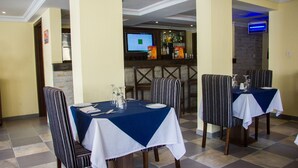 A dining area with tables set for four, striped chairs, and a bar in the background. - Sun Heaven Hotel & Resort Lekki (Lekki)