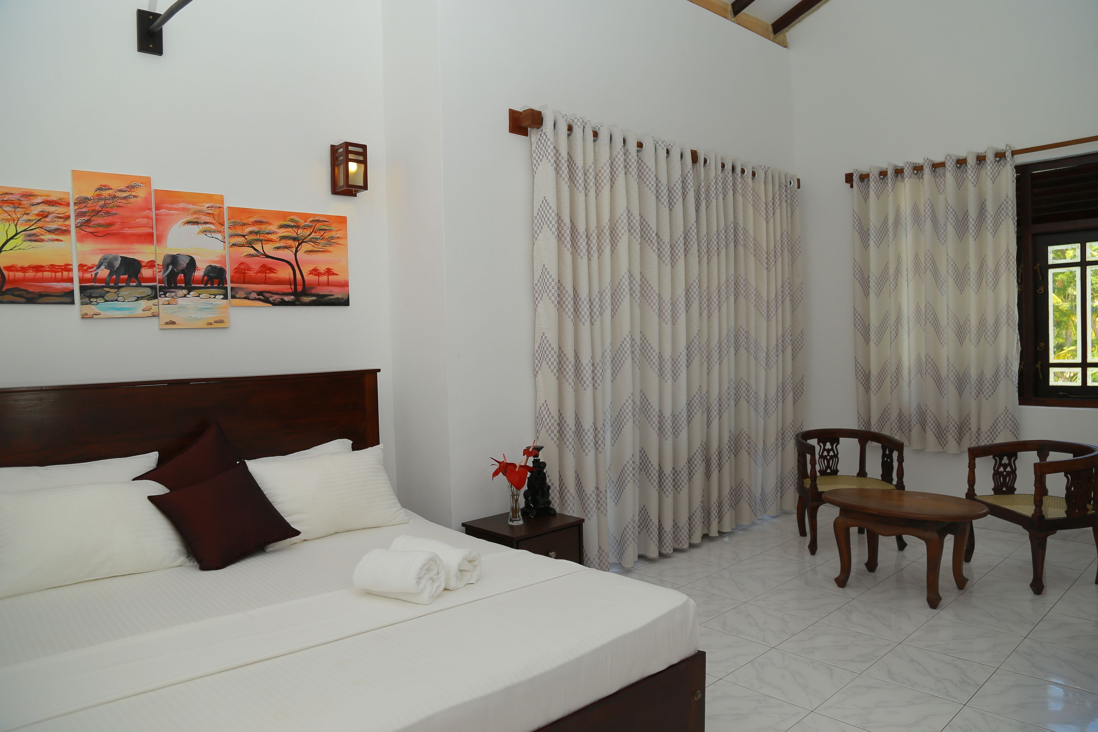 A hotel room with a large bed, two wooden chairs, a small table, and a nightstand with a vase of flowers.