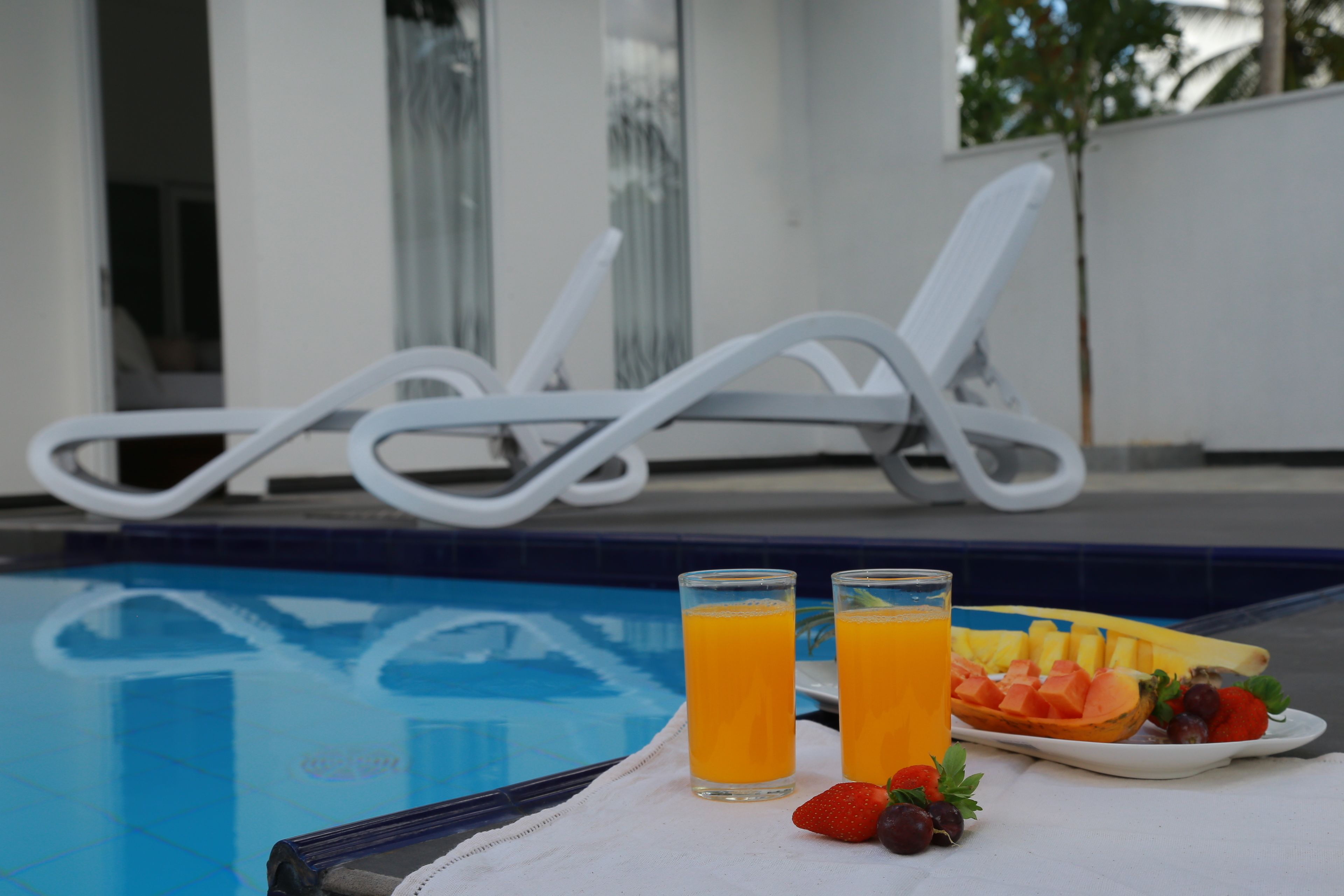 A poolside setting with two glasses of orange juice, a plate of fruit, and a white towel.