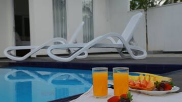 A poolside setting with two glasses of orange juice, a plate of fruit, and a white towel.