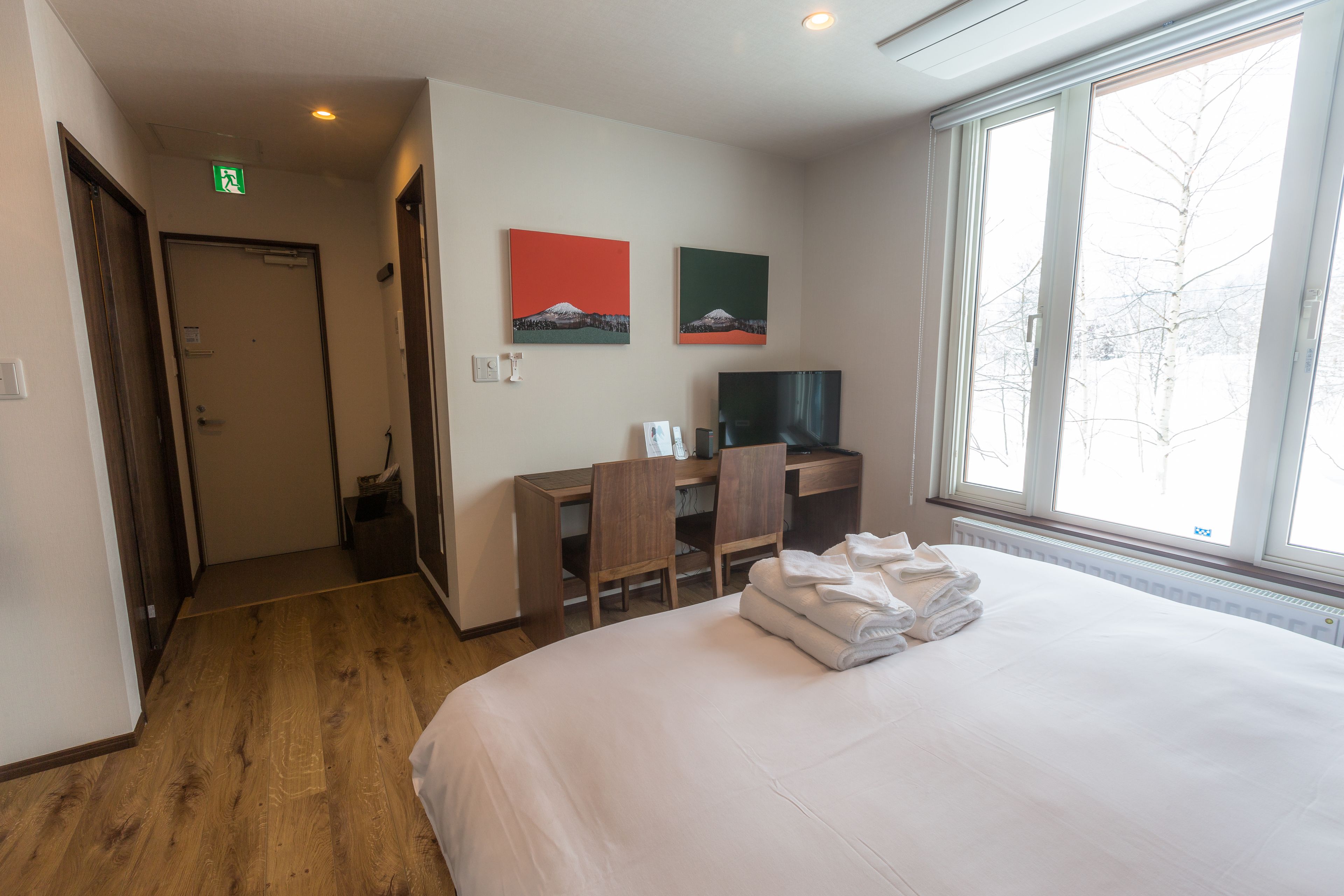 A hotel room with a bed, a desk, two chairs, a television, and artwork on the wall.
