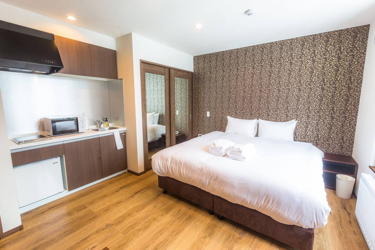 A hotel room with a bed, a small kitchenette, and a bathroom.