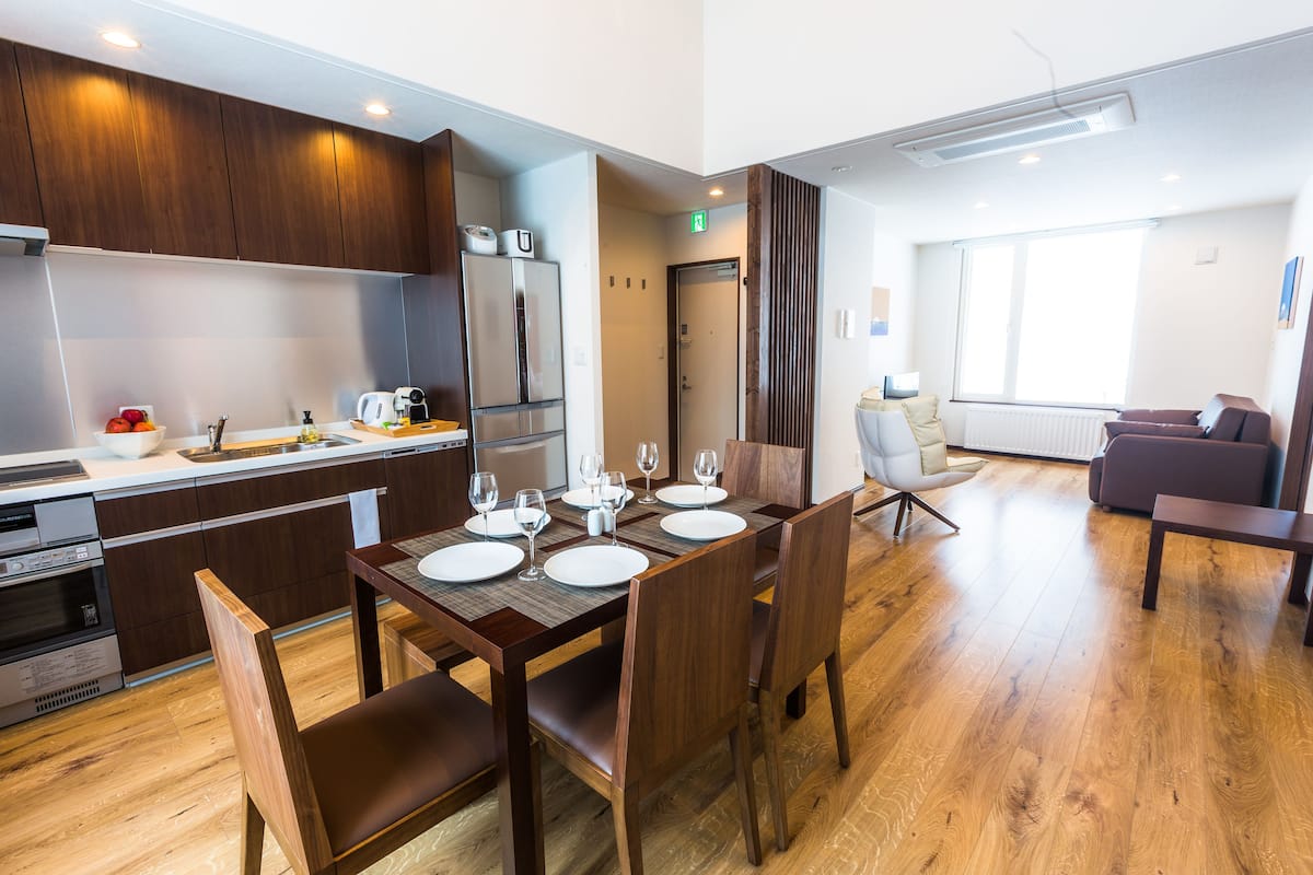 A modern kitchen with wooden cabinets, a stainless steel refrigerator, and a dining area with a wooden table and chairs.