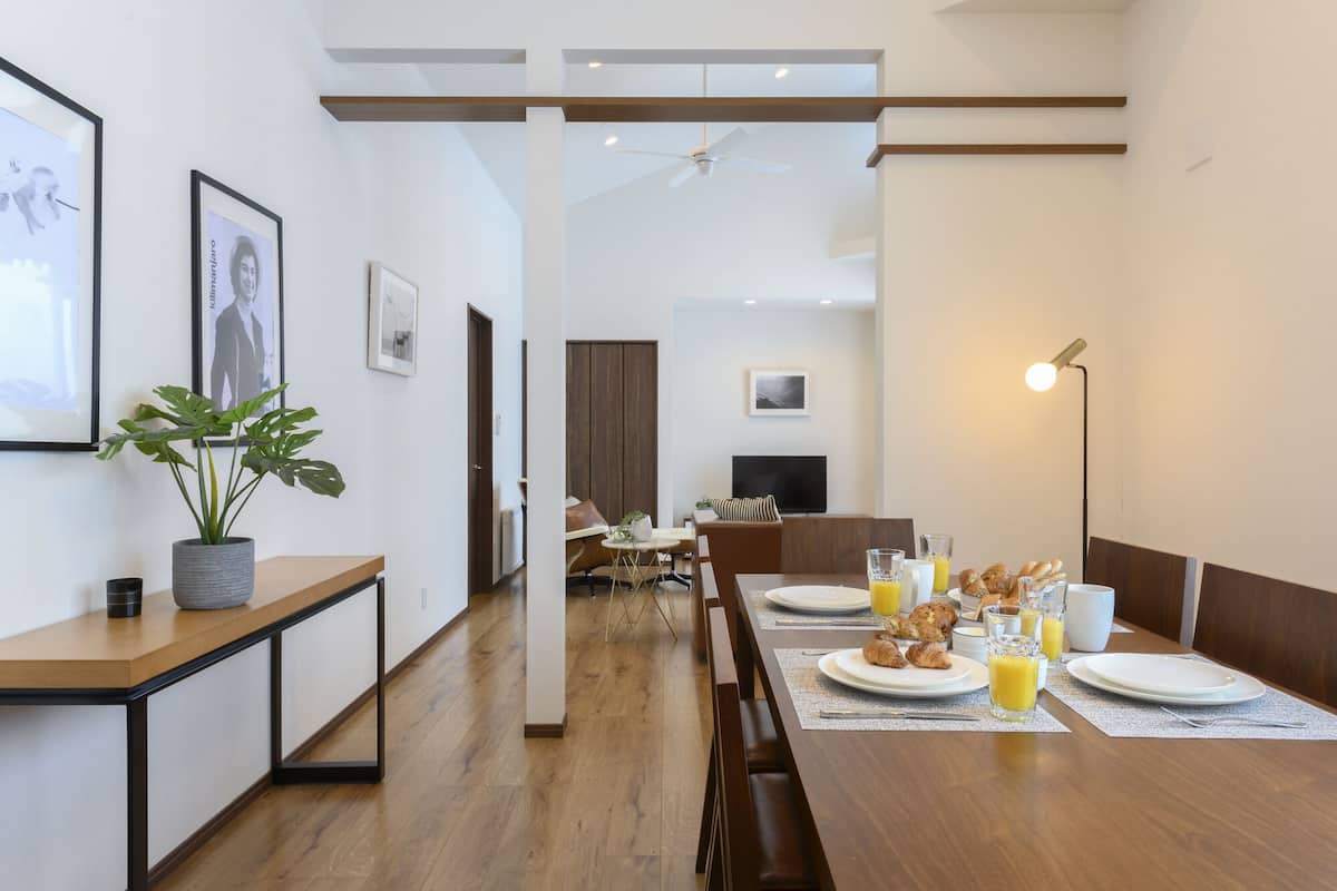 A modern dining area with a wooden table set for breakfast, a potted plant, and framed pictures on the wall.