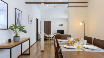 A modern dining area with a wooden table set for breakfast, a potted plant, and framed pictures on the wall.