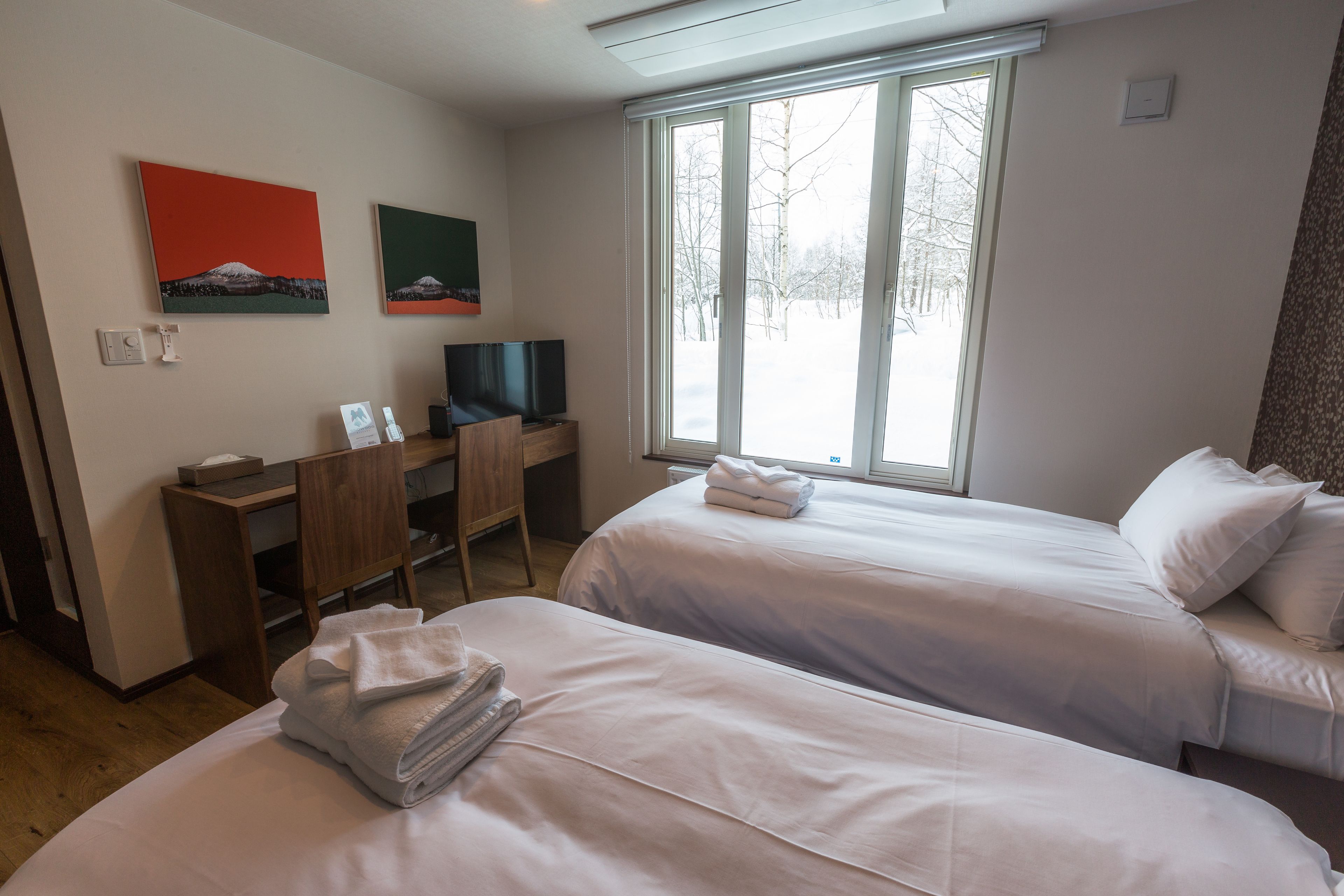 A hotel room with two beds, a desk, a chair, and a television.