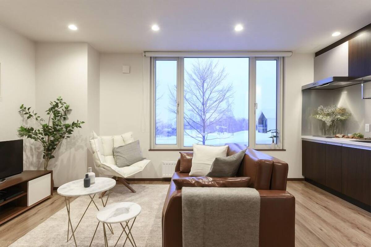A modern living room with a sofa, a coffee table, a TV, and a large window with a view of trees.