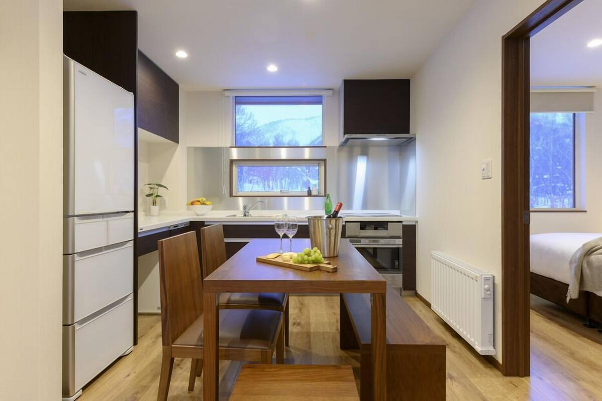 A compact kitchen with a dining table, chairs, a refrigerator, a stove, and a window.