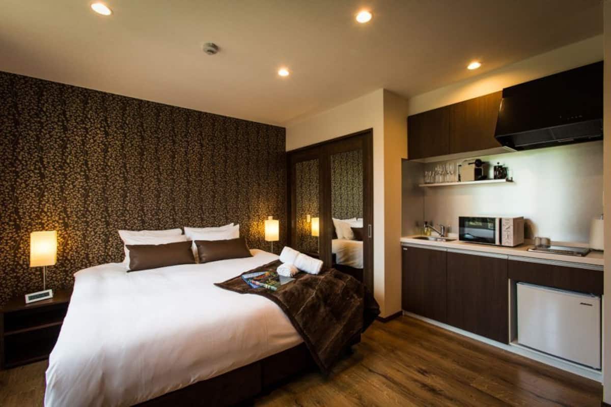 A hotel room with a large bed, a kitchenette, and a patterned wall.