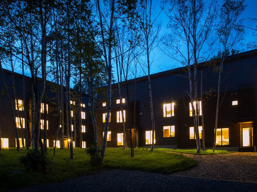 A modern building with multiple illuminated windows and a central courtyard surrounded by trees.