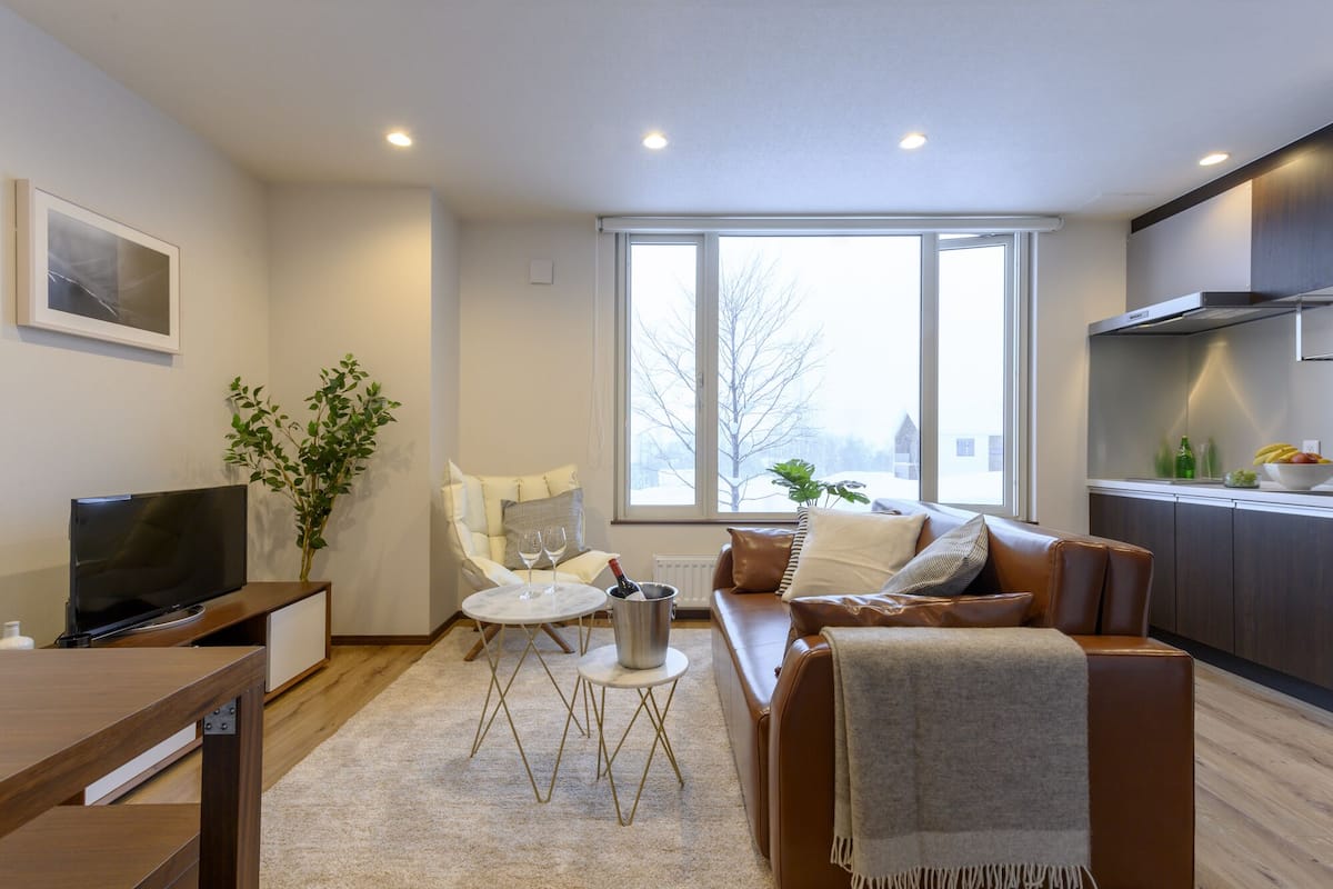 A modern living room with a sofa, a TV, a dining table, and a large window.