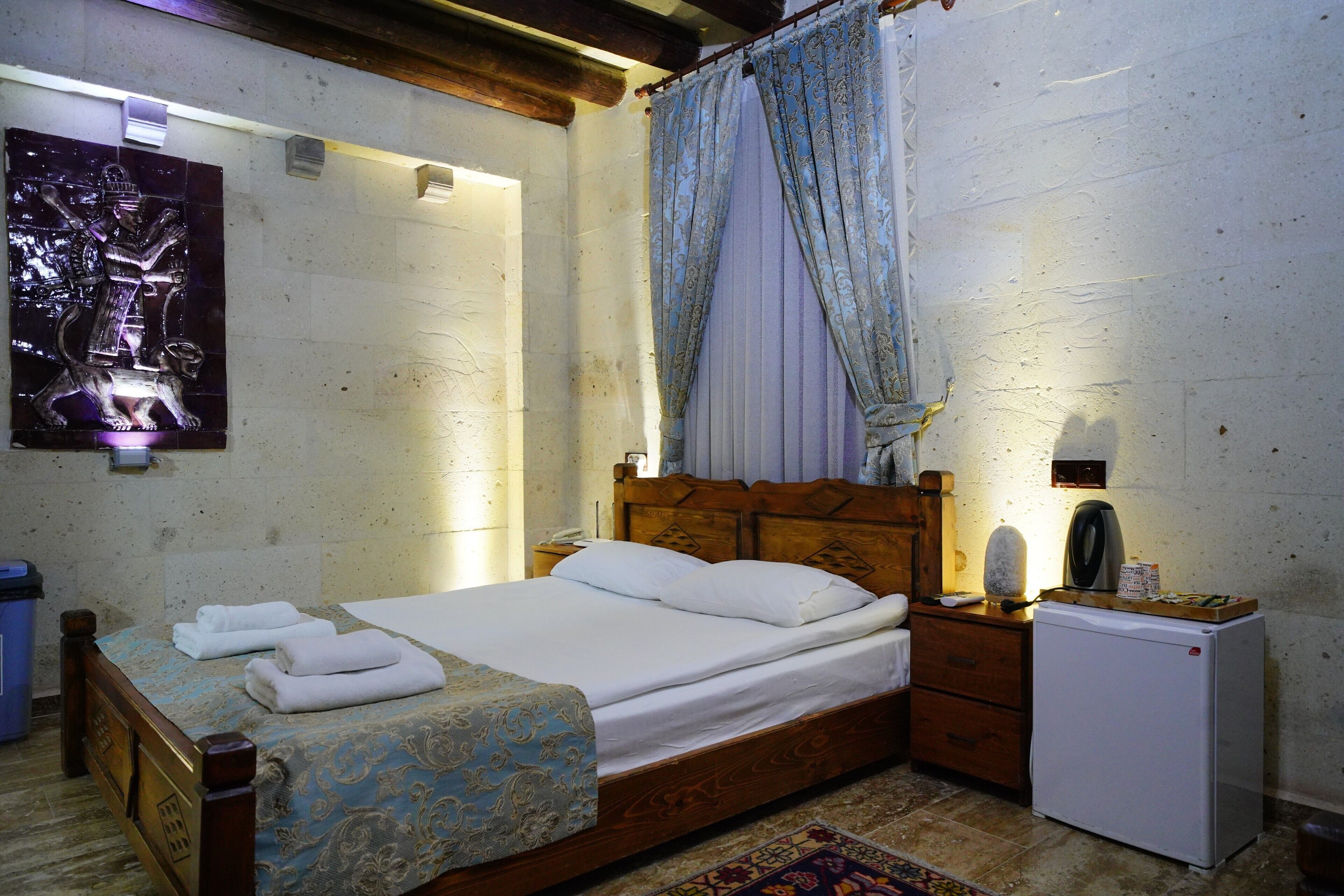 A bedroom with a wooden bed, white linens, a small refrigerator, and a nightstand.