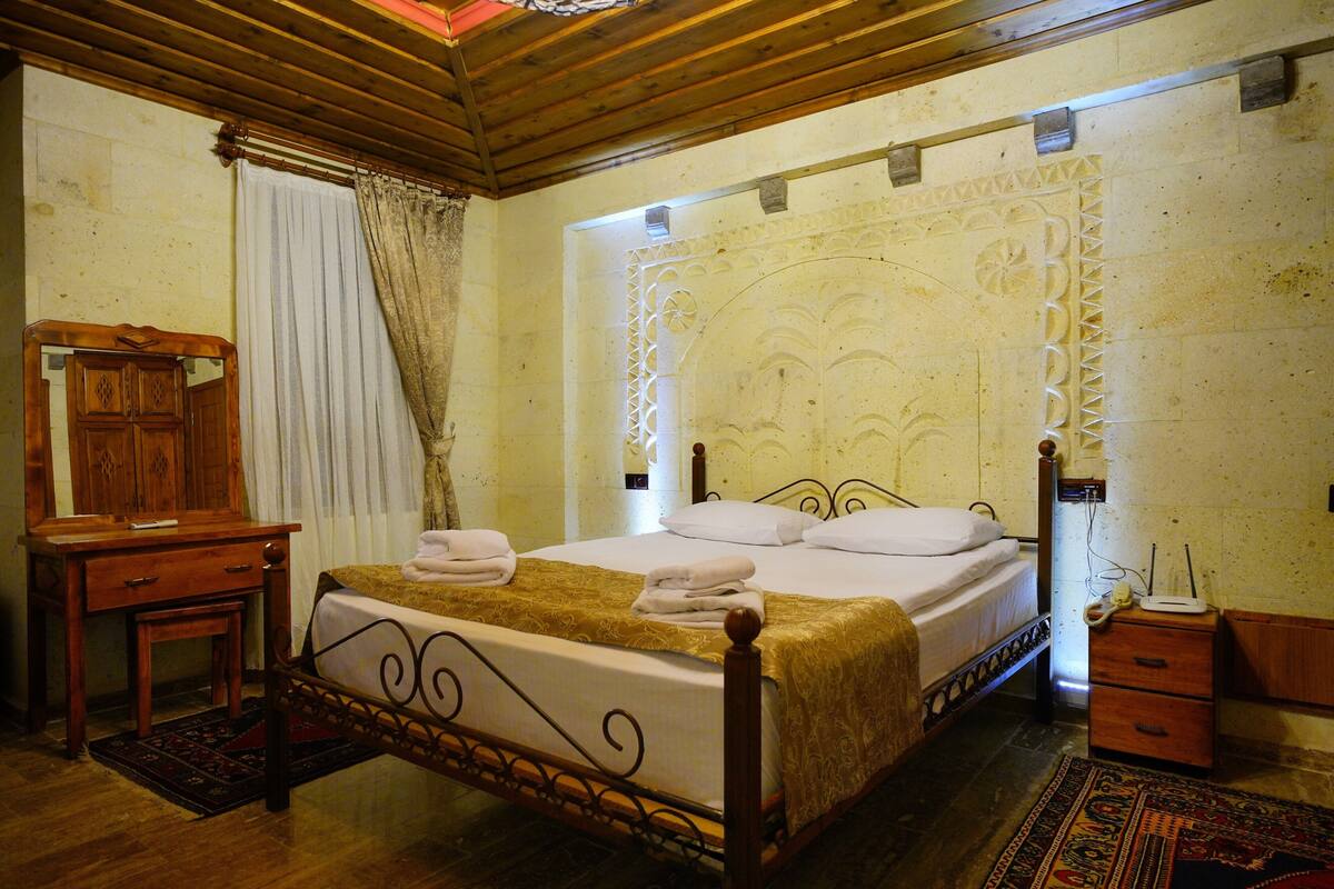 Un dormitorio con una cama de madera, una mesita de noche, un aparador y una alfombra estampada.