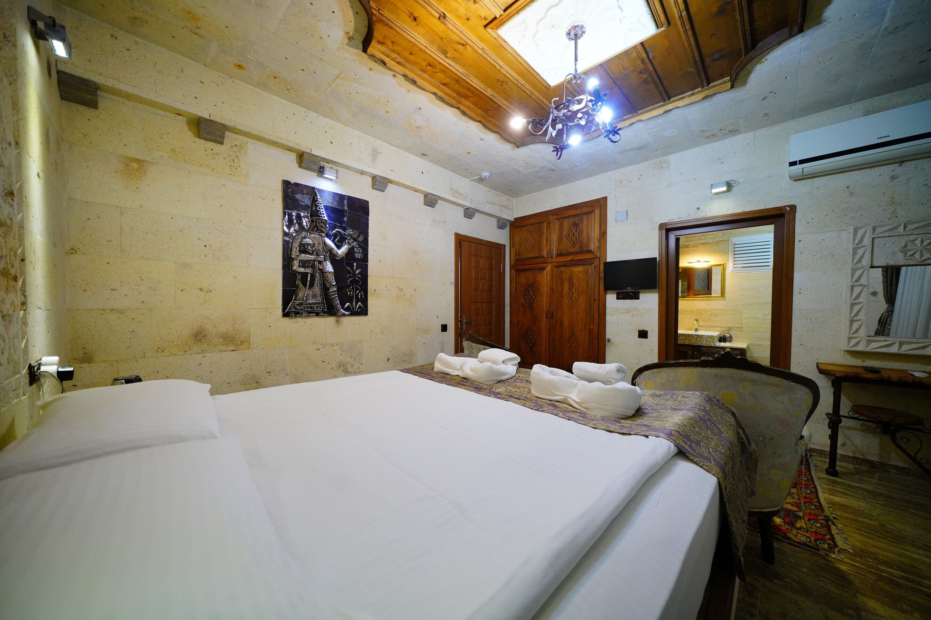 A hotel room with a large bed, wooden ceiling, and a chandelier.