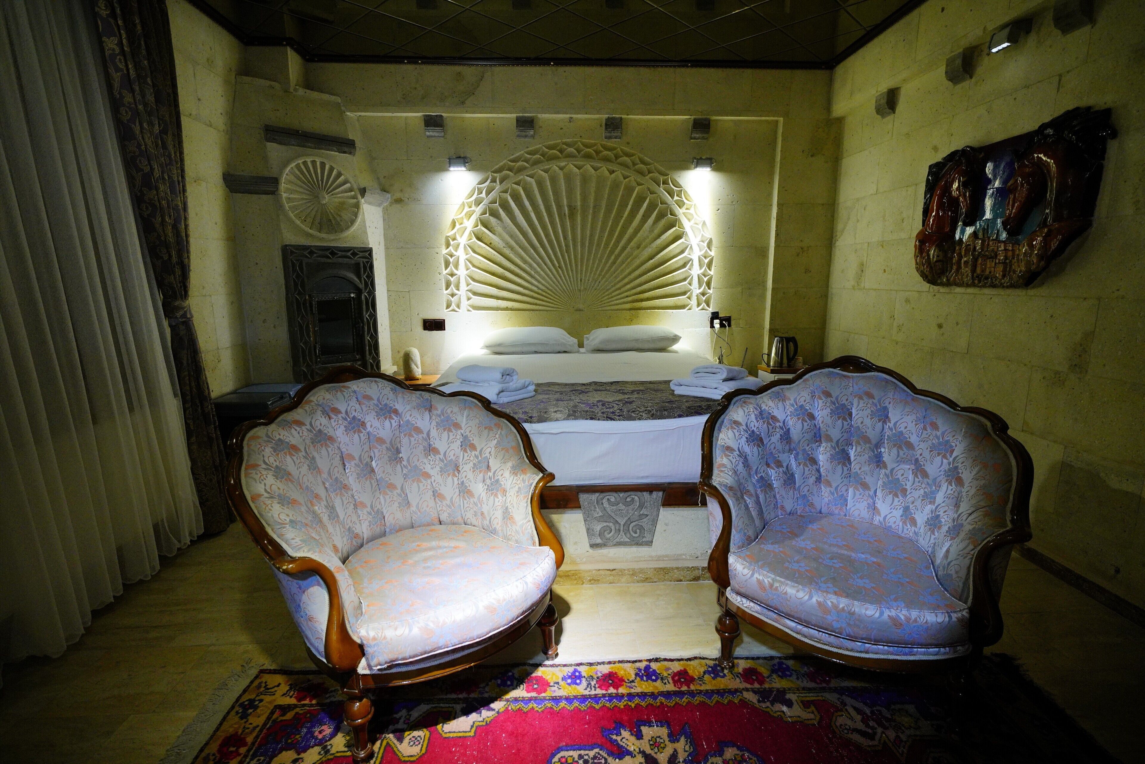 A bedroom with a large bed, two upholstered chairs, a decorative wall, and a patterned rug.