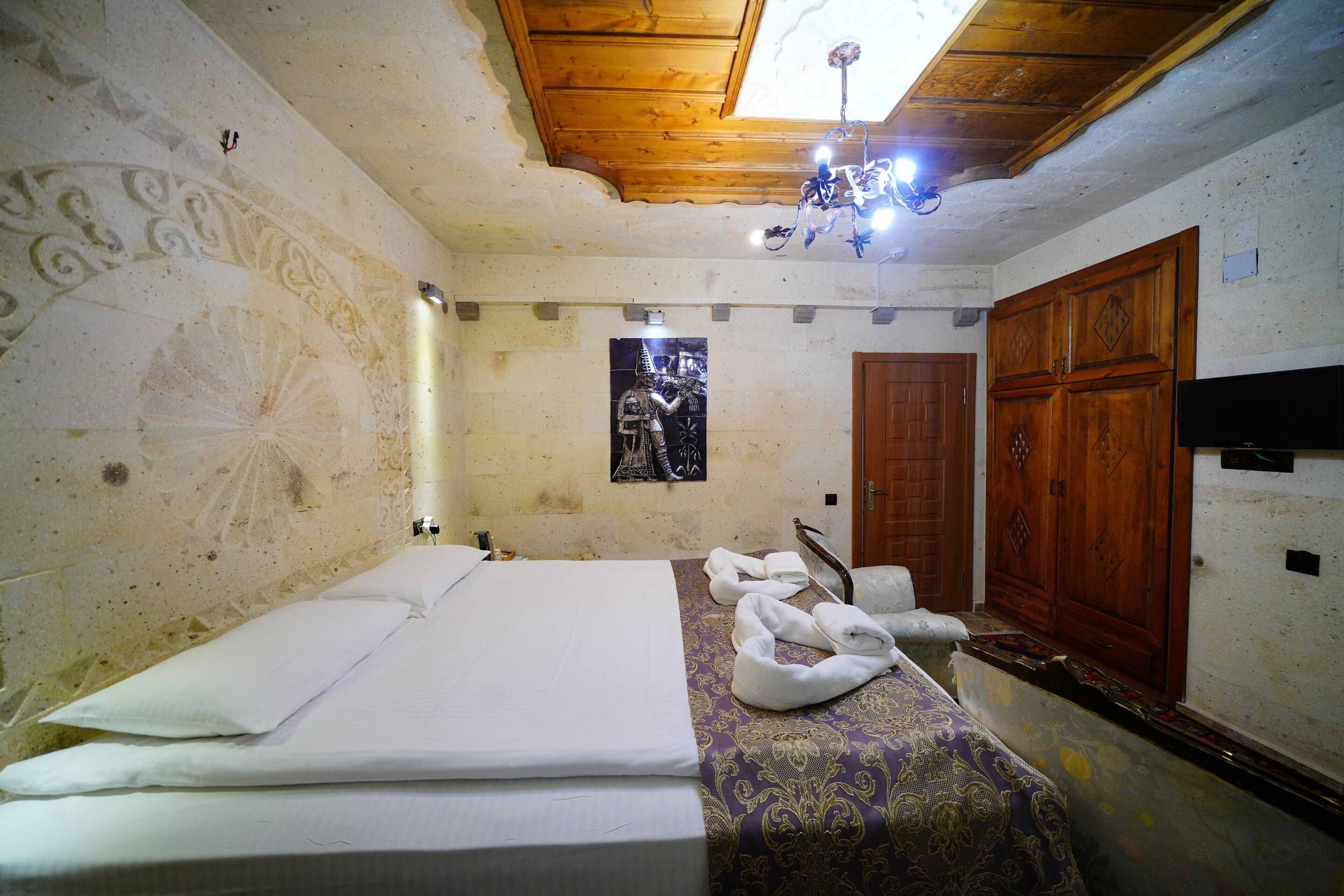 A room with a bed, towels, a wooden wardrobe, and a wall-mounted TV.
