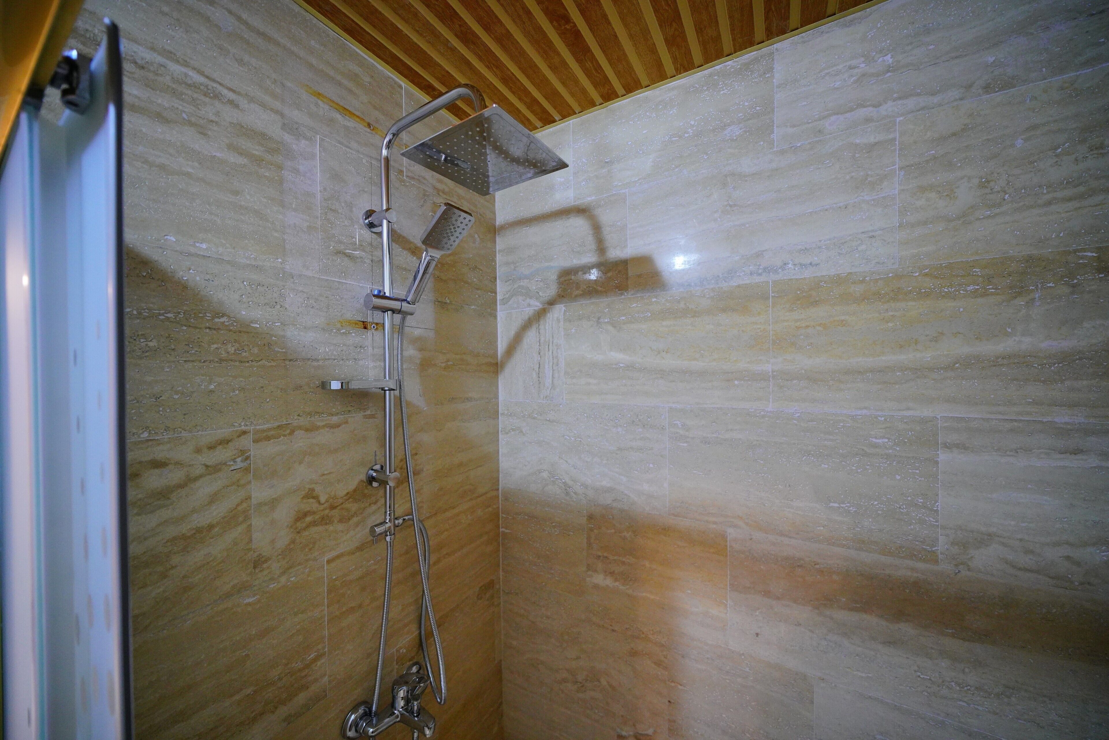 A shower with a handheld showerhead and a fixed showerhead, tiled walls, and a wooden ceiling.