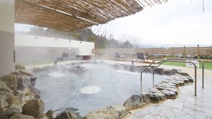 Un área de aguas termales con escalones de piedra que bajan al agua, una pérgola de madera en la parte superior y vistas de montañas al fondo.