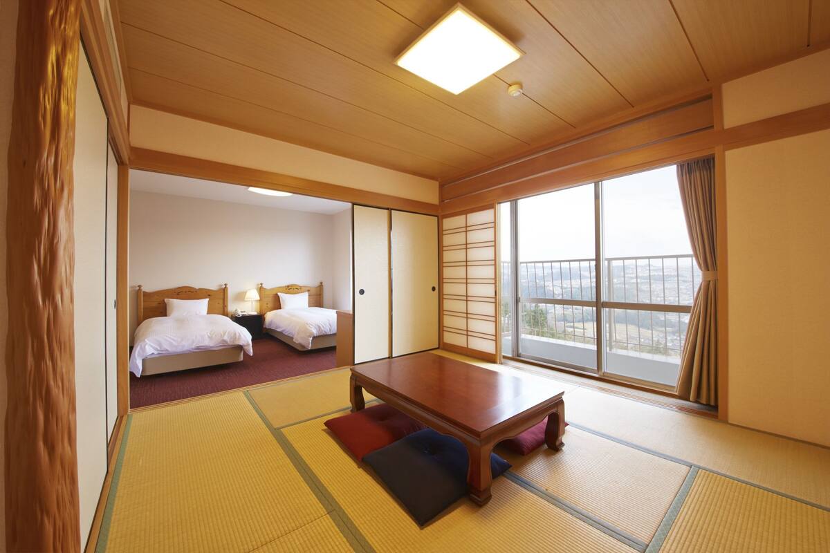A traditional Japanese room with tatami flooring, a wooden table, and a large window with a view.