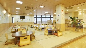 Un comedor amplio con múltiples mesas y sillas, ventanas grandes y vistas a la ciudad.