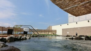 Un área de aguas termales con una terraza de madera, una escalera metálica y un edificio al fondo.
