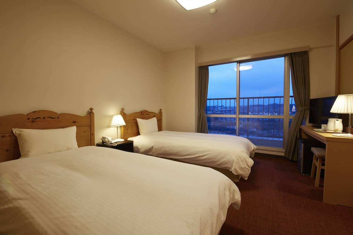 A hotel room with two beds, a desk, a chair, a TV, and a large window with a view.