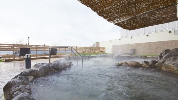 Un área de aguas termales con una terraza de madera, asientos de piedra y un paseo cubierto.