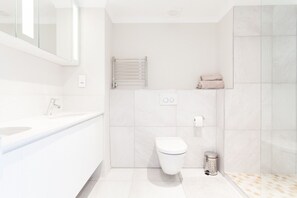 A modern bathroom with a white sink, a toilet, a towel rack, and a trash can.