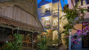 A traditional building with a thatched roof and a modern structure with balconies and potted plants.