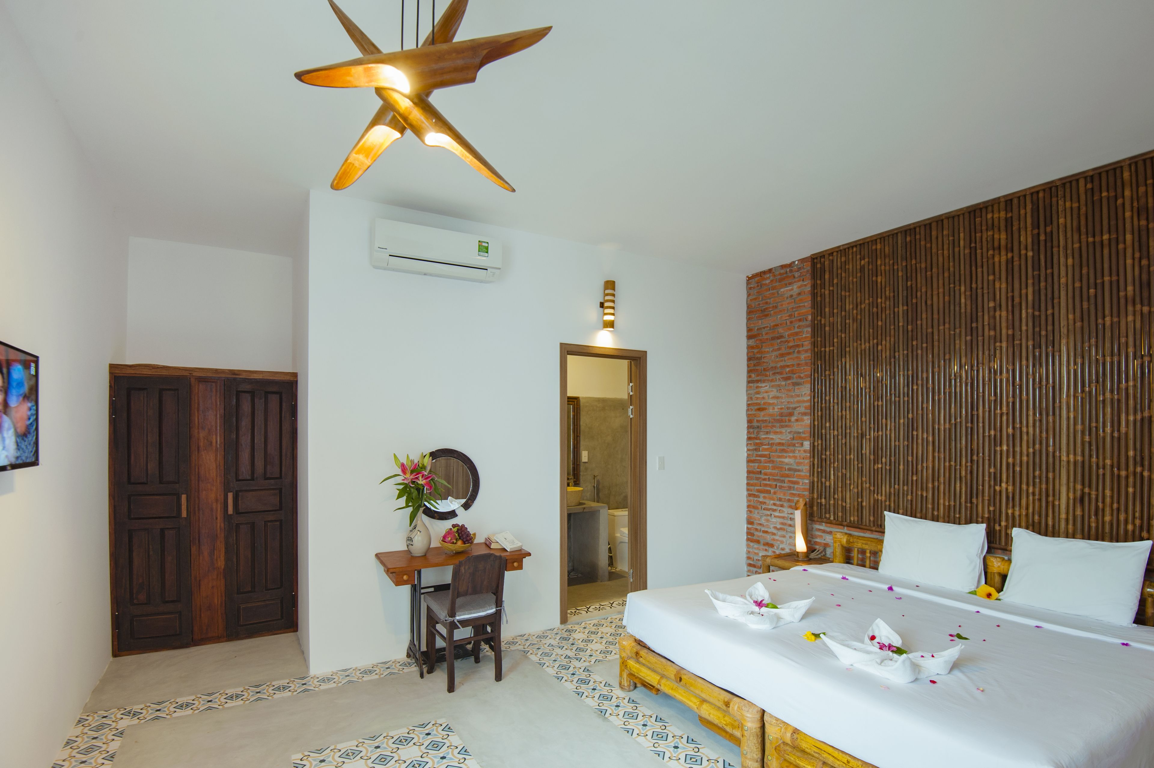 Une chambre d’hôtel comprenant un lit, un bureau avec une chaise, un miroir et un ventilateur de plafond.
