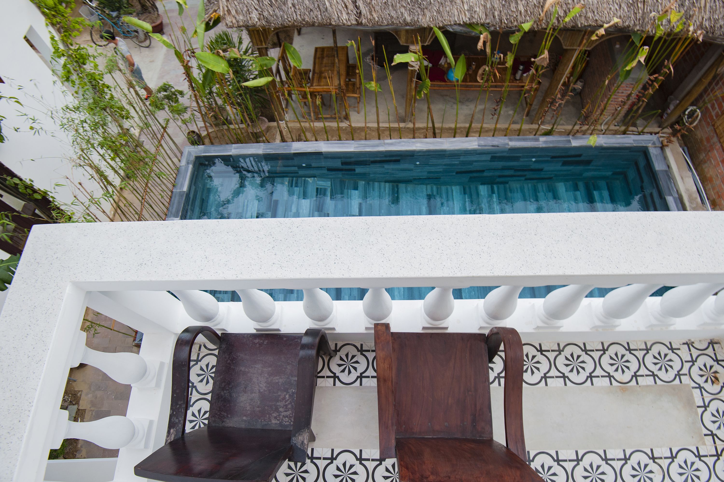 A pool with a white balustrade and a tiled area with a chair and table.