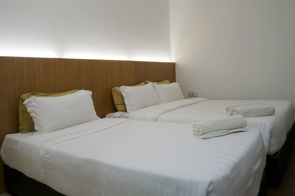 Ett hotellrum med två sängar, vita sängkläder och en sänggavel i trä.