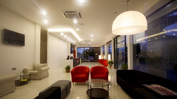 A modern hotel lobby with a reception desk, seating area with sofas and armchairs, and large windows offering a view of the cityscape. - Place2Stay Business Hotel - Waterfront (Kuching)