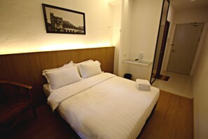 Un lit bien fait, avec du linge de lit blanc, une tête de lit en bois et un tableau encadré accroché au mur.