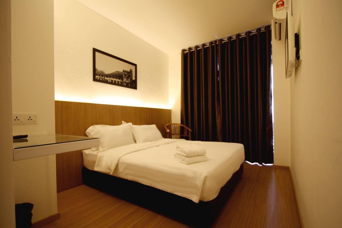 Ett hotellrum med en säng, en stol, ett skrivbord och en väggmonterad luftkonditioneringsanläggning.