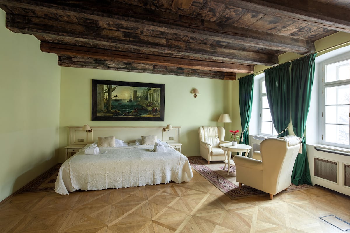 A room with a bed, a chair, a table, and a painting on the wall.