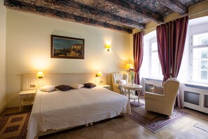 Une chambre d’hôtel avec un grand lit, deux lampes de chevet, une chaise, une petite table et un tableau au mur.