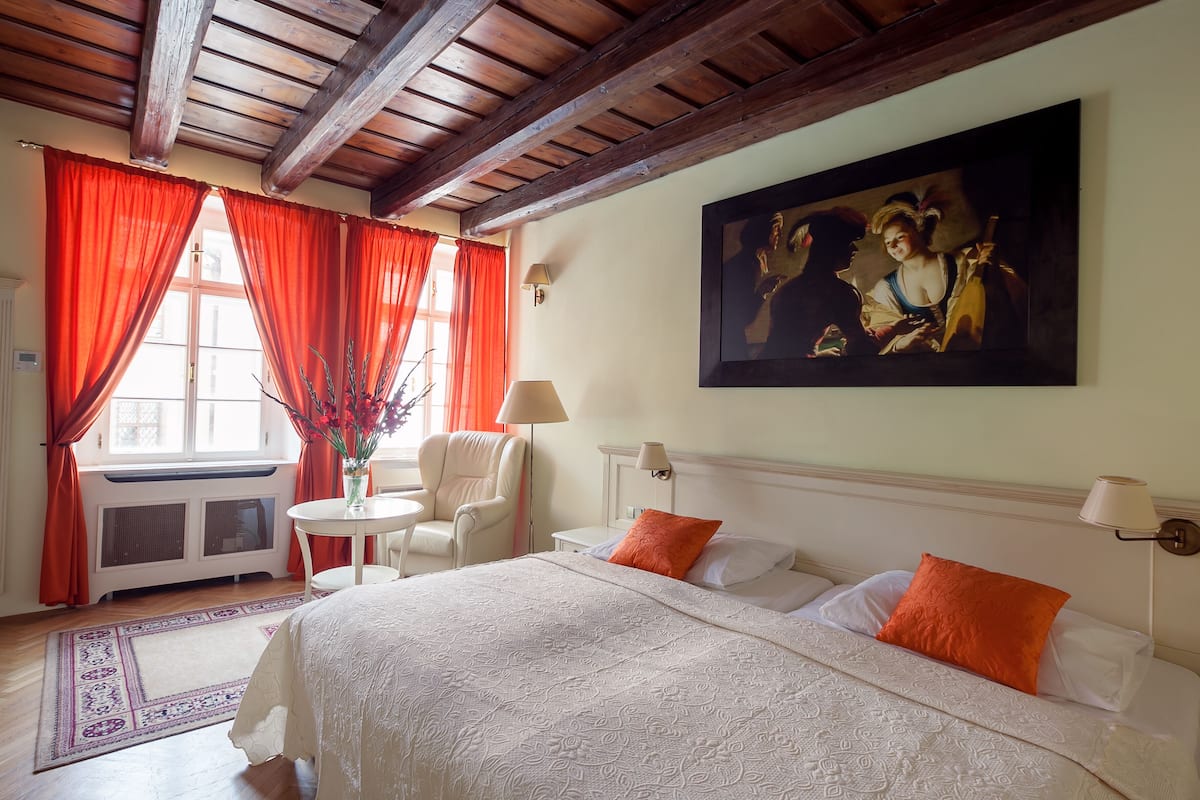 A hotel room with a bed, a chair, a table, and a painting on the wall.