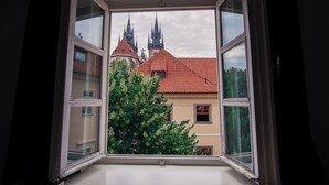 A view through a window of a building with a red-tiled roof and two spires, likely a church or cathedral, with a tree in the foreground. - Tyn Yard Residence (Prague)