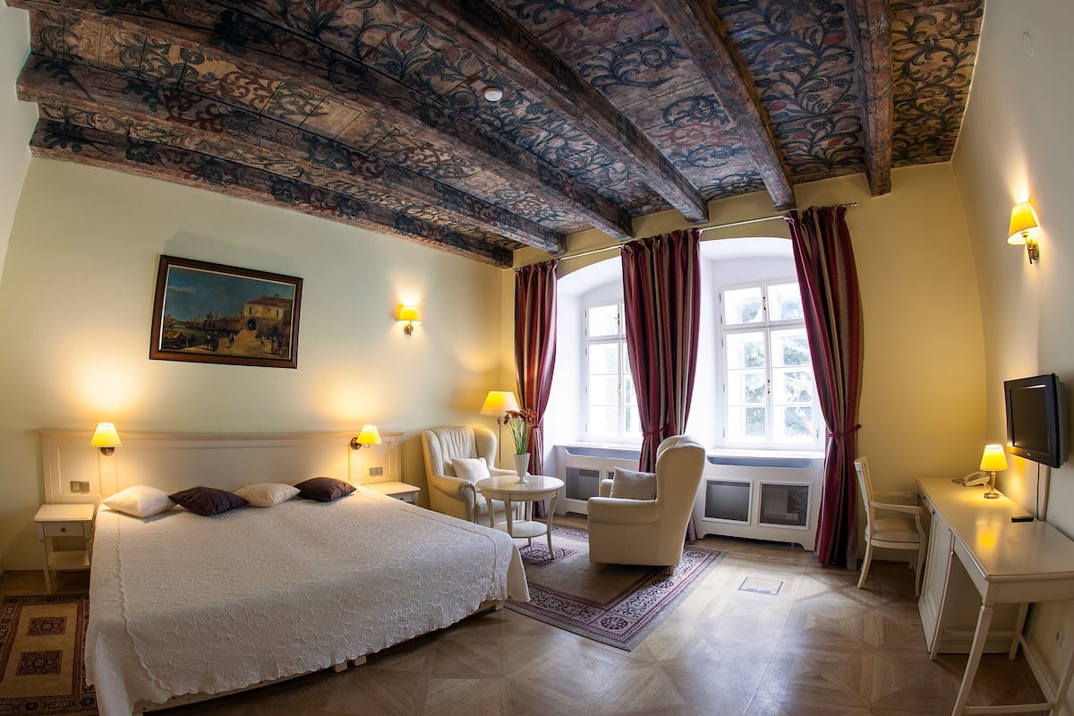 A hotel room with a large bed, a desk, a chair, and a TV.