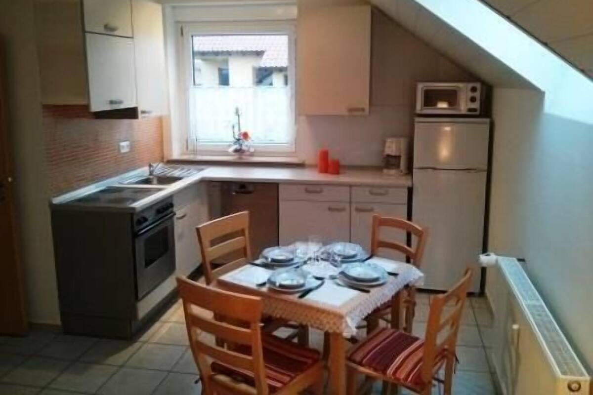 Una cocina compacta con una mesa de comedor para cuatro personas, microondas y ventana que proporciona luz natural.