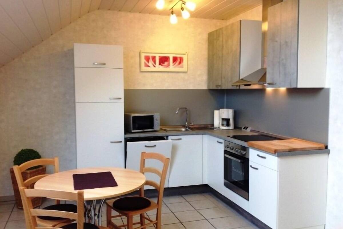 Cocina compacta con armarios blancos, microondas, cafetera y una mesa de comedor con sillas.