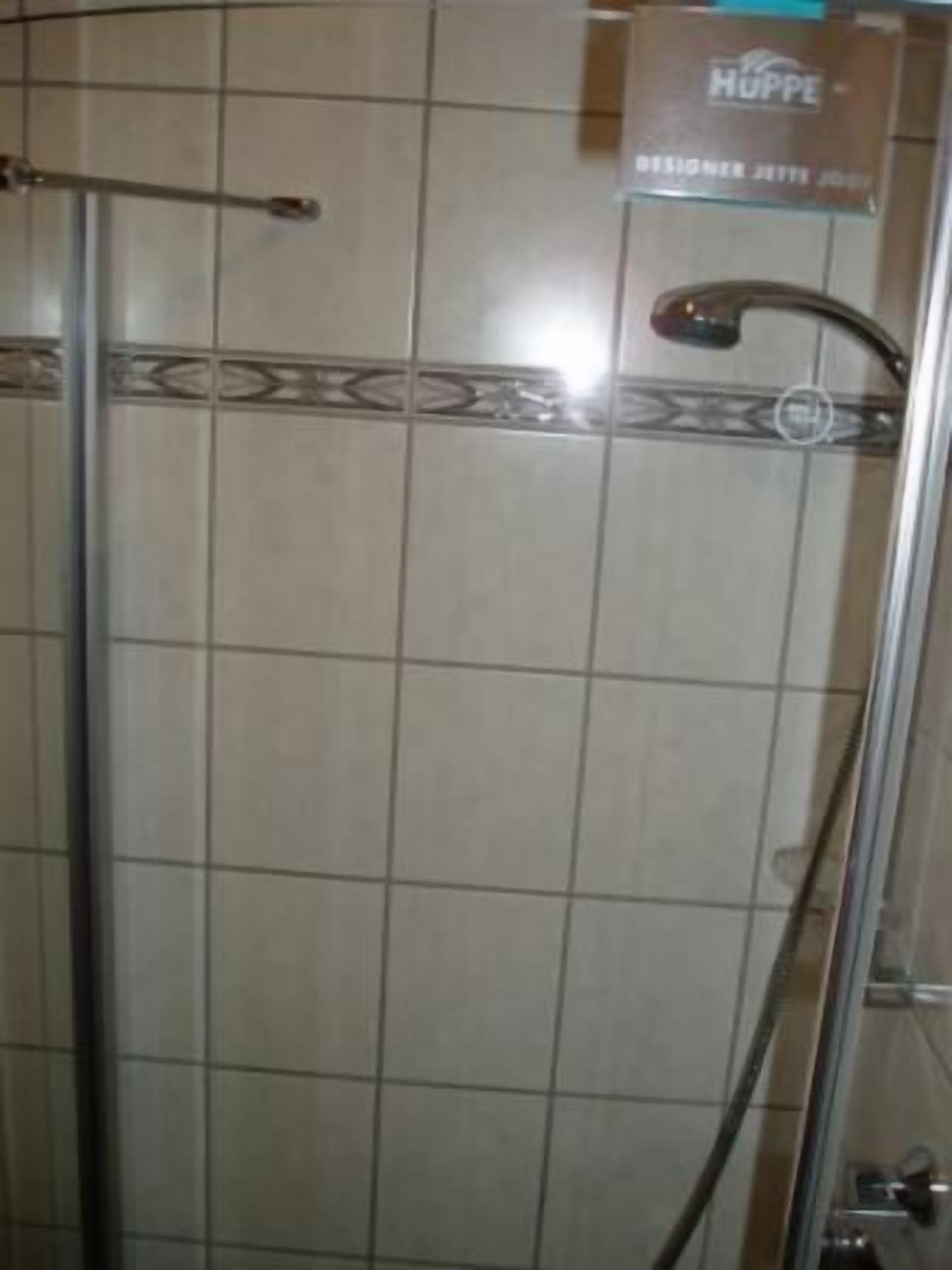 Eine Dusche mit Glastür, Metallgriff und einem Schild mit der Aufschrift 'HUPPE DESIGNER JETTY JO'.