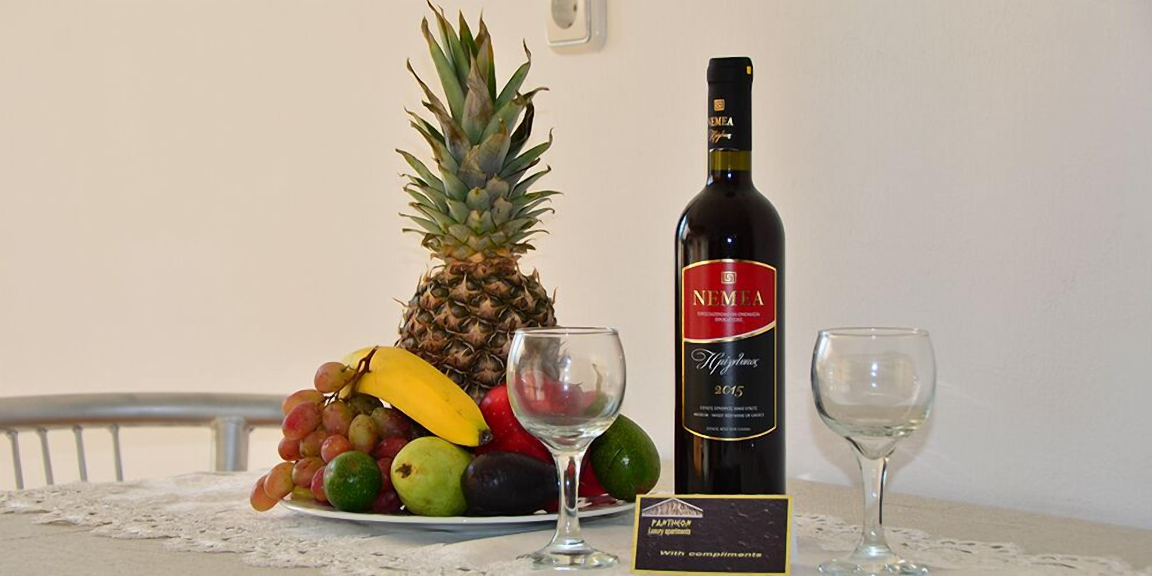 A table with a bottle of wine, two glasses, and a plate of fruits.