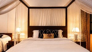 Een groot bed met hemel, twee nachtkastjes met lampen, en een gordijn met patroon.